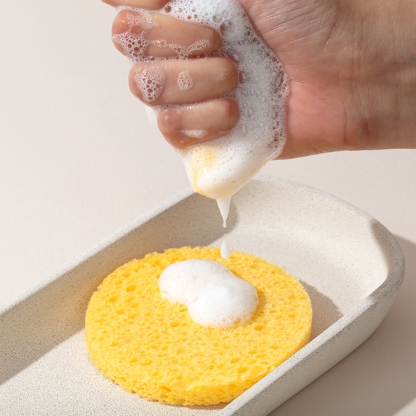 skc2008_1 Hand squeezing the Foaming Cleanser onto the Facial Cleansing Sponges placed in a speckled tray