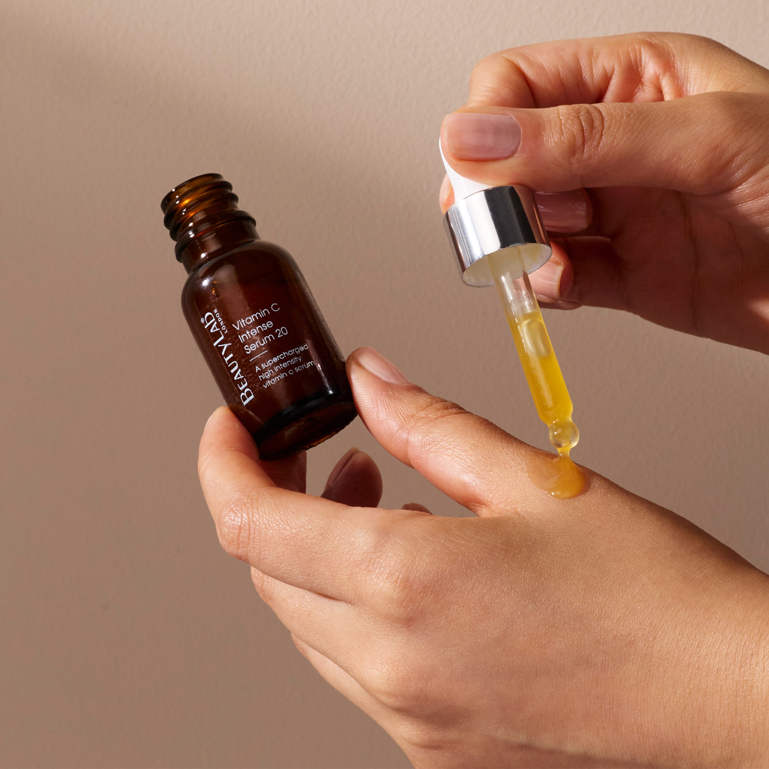 Model holding a bottle of Vitamin C Intense Serum 20 and using the dropper to dispense serum onto her hand