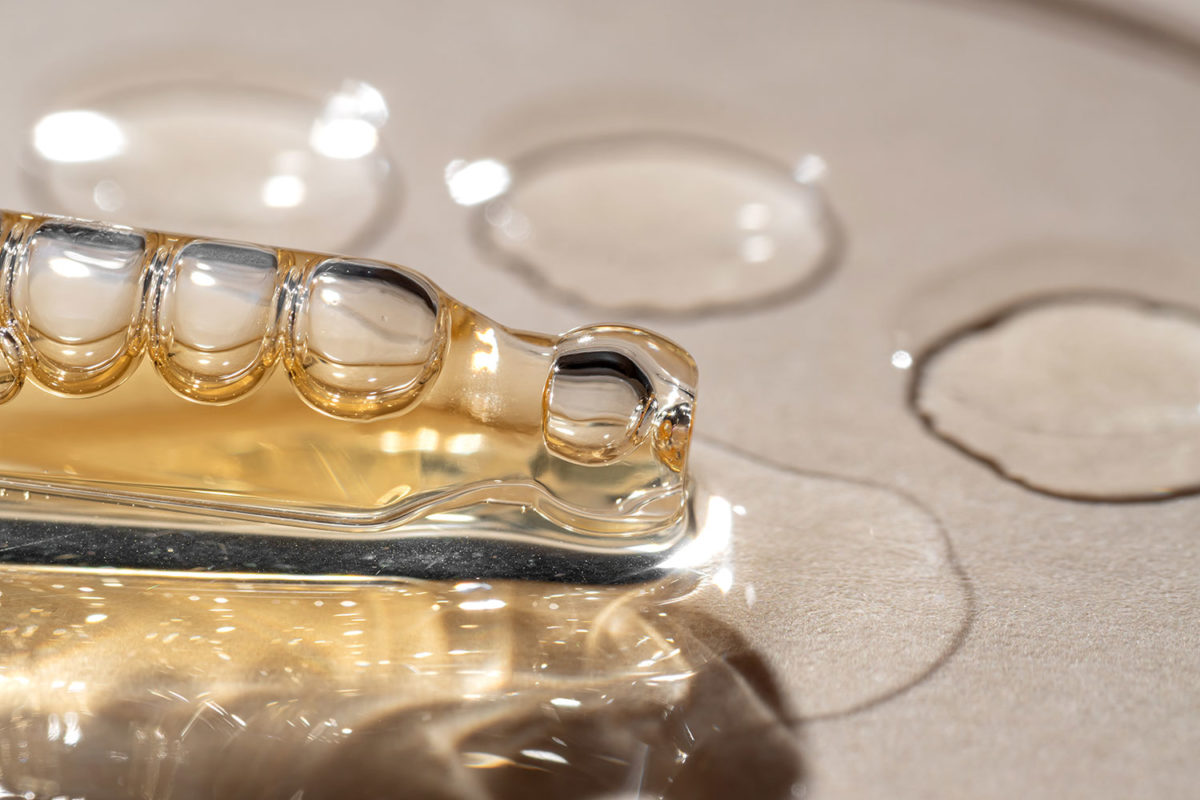 Close-up of a glass serum dropper resting on a surface with several droplets of serum.